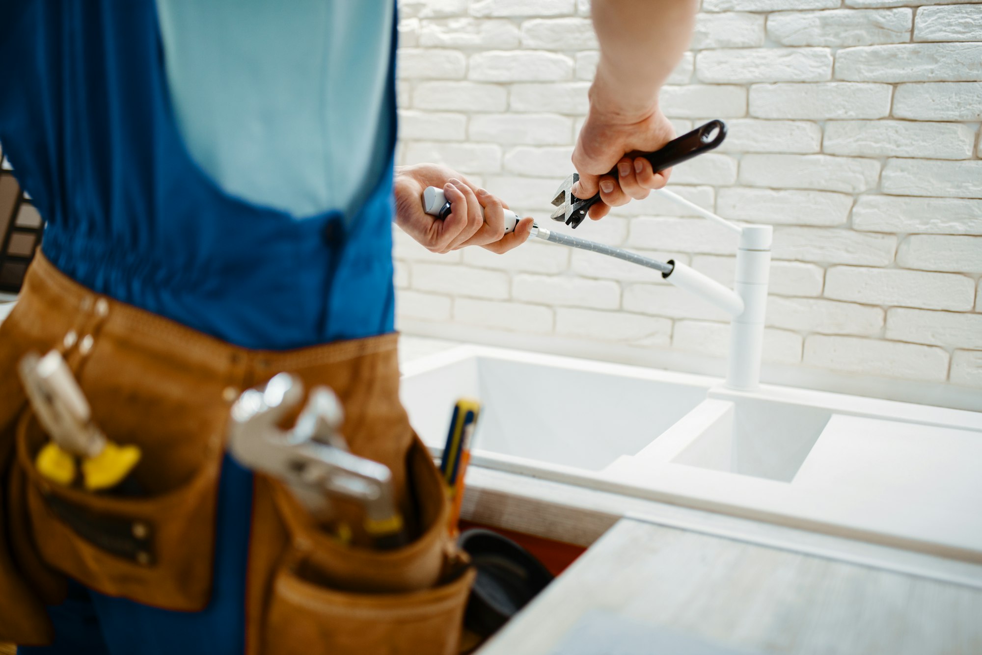 Plumber in uniform fixing faucet in the kitchen