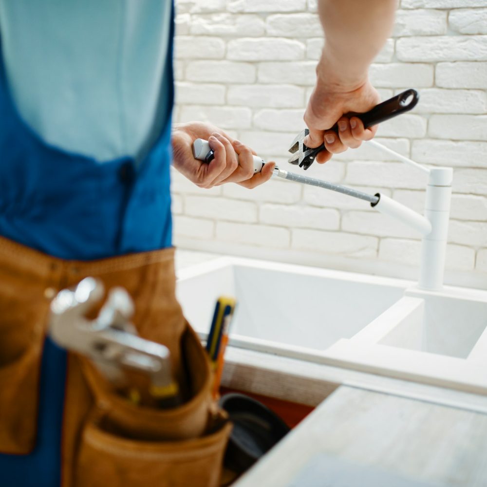 Plumber in uniform fixing faucet in the kitchen